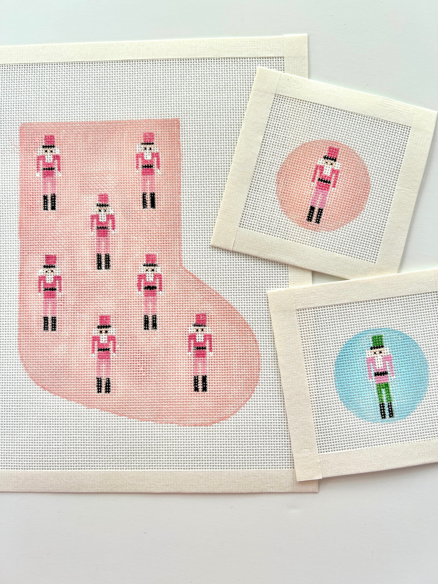 Mini nutcracker stocking in pink shown with round mini bag charms needlepoint canvases in pink and blue on white background.