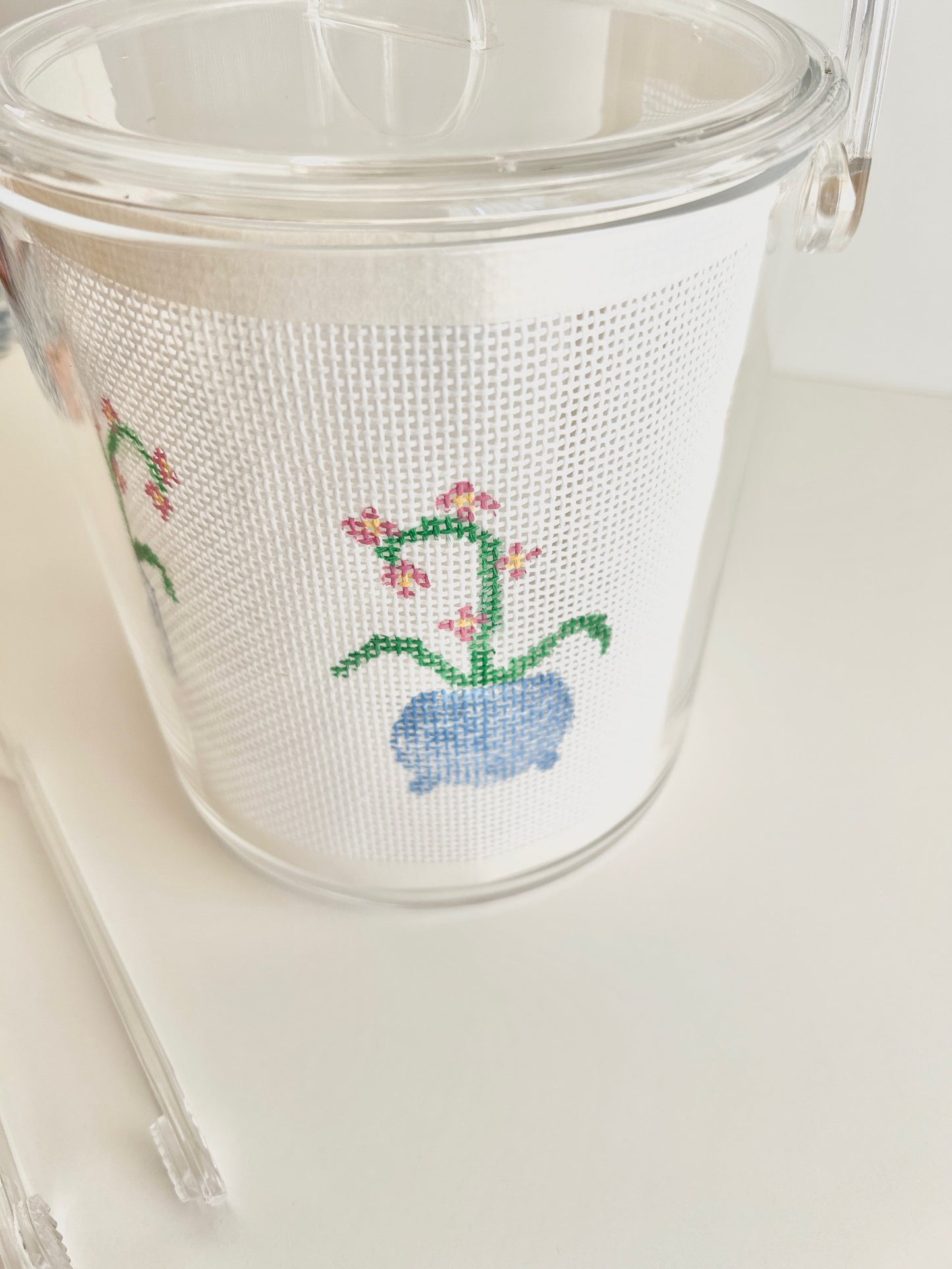 Clear acrylic ice bucket with needlepoint design of orchid on a white background