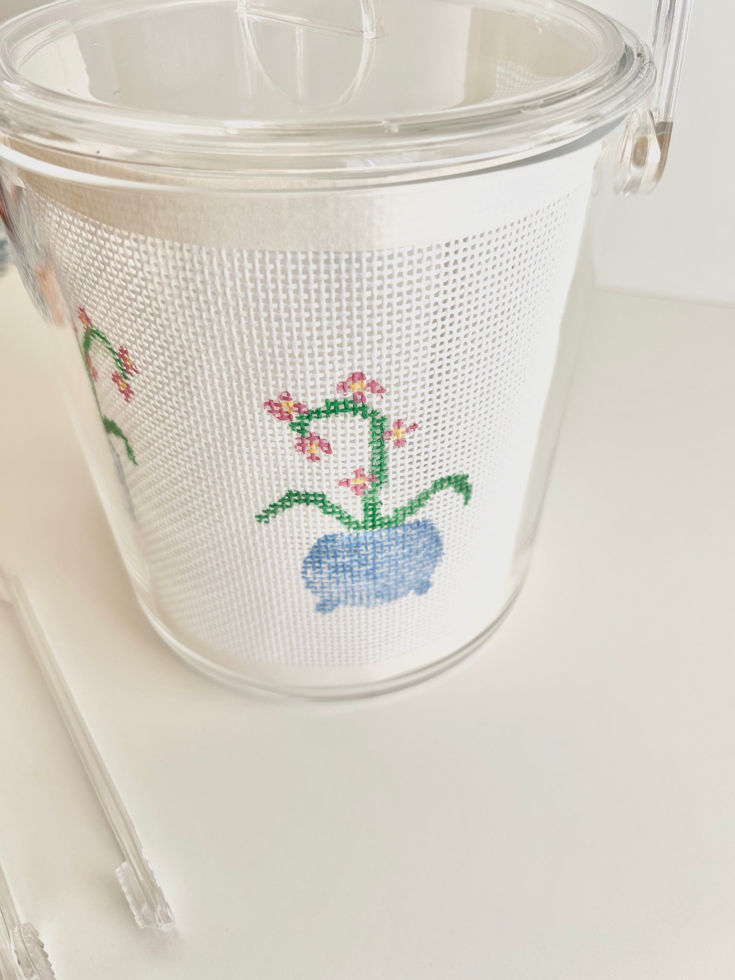 Clear acrylic ice bucket with needlepoint design of orchid on a white background