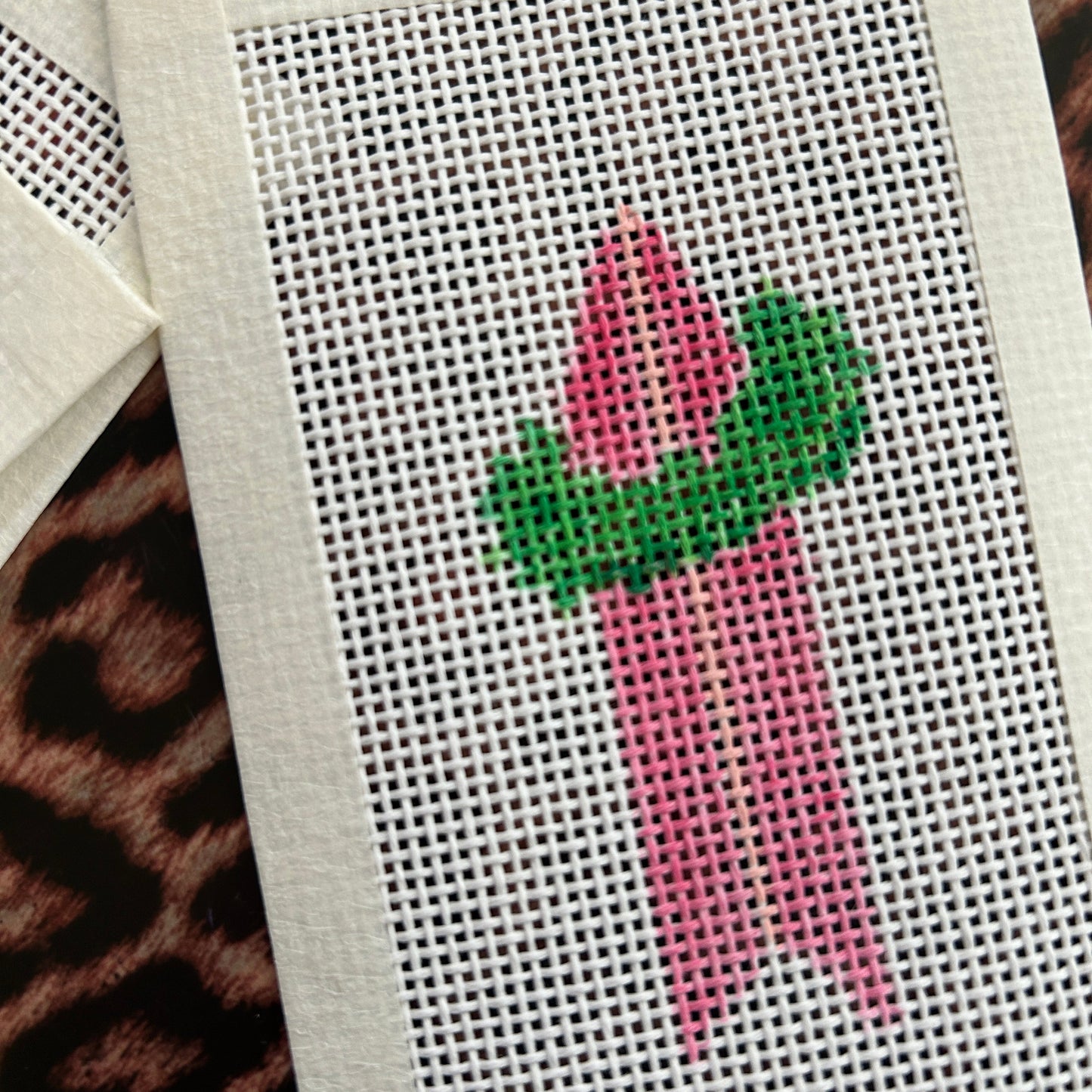 Needlepoint design of a pink surfboard with a green wreath.