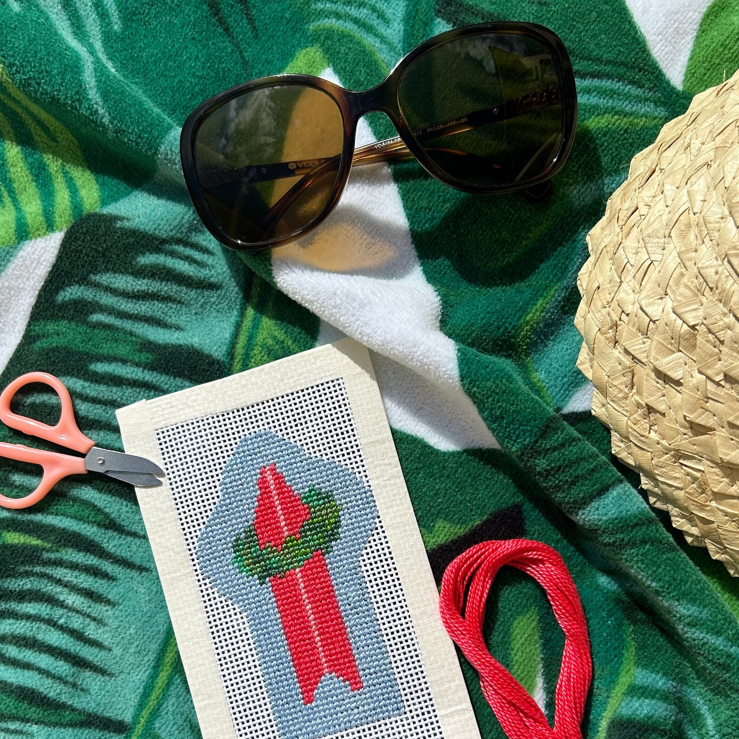 Holiday surfboard needlepoint canvas with wreath on a beach towel with hat and sunglasses. 