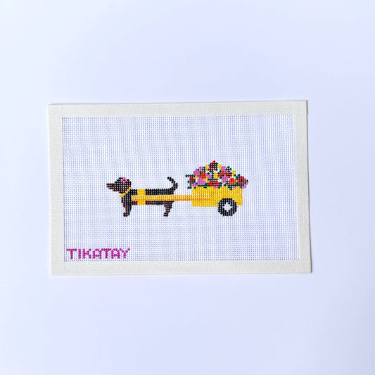 A dachshund pulling a yellow flower cart needlepoint canvas by tikatay on a white background.