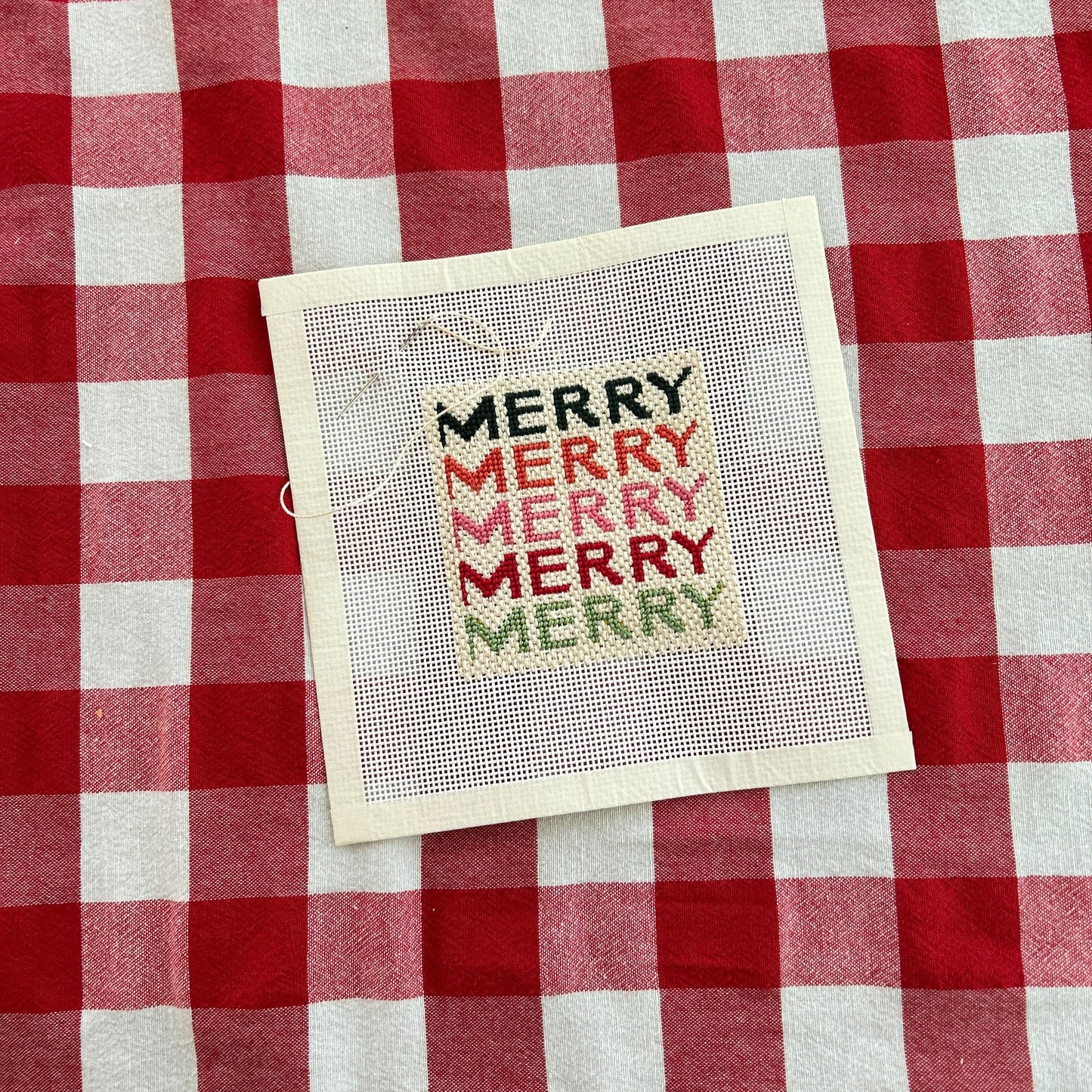 Needlepoint canvas featuring the words Merry in pinks, reds and greens in a modern font.