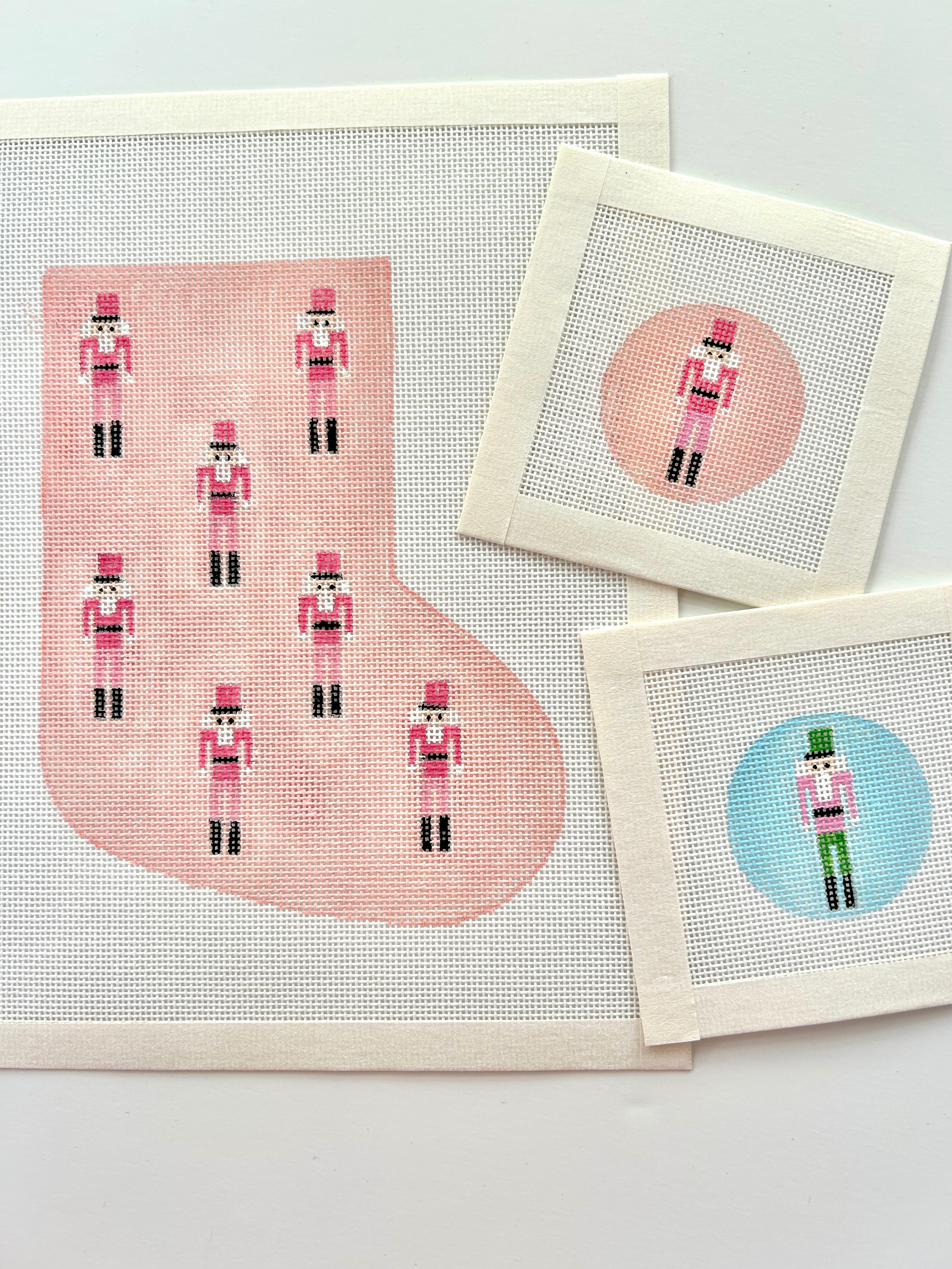 Mini nutcracker stocking in pink shown with round mini bag charms needlepoint canvases in pink and blue on white background.