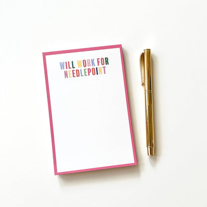 Paper notepad with 'Will work for needlepoint' text and a pen on a white background